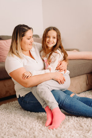 Photo of two persons mother and daughter passing time together at home sitting on the carpet, mother holding her little girlon her knees.の写真素材