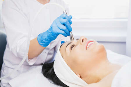 Cropped photo of beautician anhd happy woman lying on the massage table and getting procedure microdermabrasion by a beautician in blue gloves in a cosmetologist clinic.の写真素材