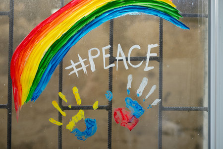 Colorful photo of handprints in paint of two flags Russia and Ukraine on window with bars and inscription of peace with rainbow.の写真素材