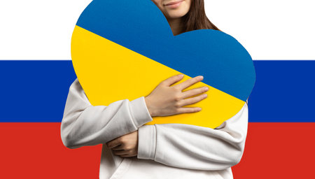 A girl holds a heart to her chest with the flag of Ukraine, and behind her the flag of the Russian Federation.の写真素材