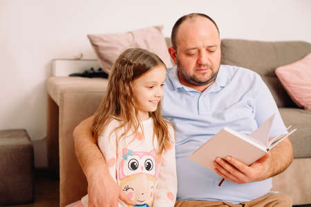 Lovely family of two persons father and his daughter in living room at home reading interesting book fairy tale.の写真素材