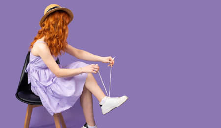 Side view photo of a redhead young pretty woman in sundress and strae hat holds shoelaces in hands...