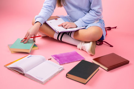 Cropped photo of a young school girl sitting on the floor with crossed legs and with books around her, education in high school concept.の写真素材