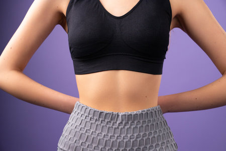Cropped photo of a young woman having slim body wearing black top holding her hands in the back posing on purple background.の写真素材