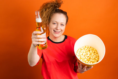 Woman football fan cheering and supporting her football team with a bottle of beer and popcorn holding in her hands.の写真素材
