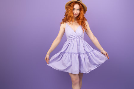 Amazing beautiful redhead girl with blue eyes wearing a straw hat and holding the sundress with both hands at the sides.の写真素材