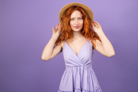Portrait of beautiful redhead woman with fresh makeup and romantic hairstyle in violet dress with straw hat on her head.の写真素材