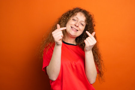 Joyful beautiful redhead woman in red t-shirt keeping her fingers crossed as a luck for football team in the championship.の写真素材