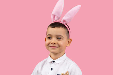 Close up photo of a little boy in white t-shirt wearin bunny earson head smiling and posing on pink background, Easter concept holiday.の写真素材