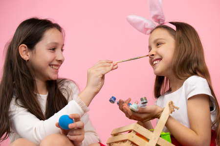 Close up photo of lovely girls making fun painting nose and wearing bunny ears, preparing for theEaster holiday.の写真素材