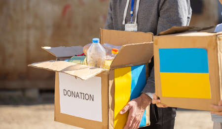 Close up photo of volunteer carrying box with humanitarian aid for ukrainian refugees in street, helping people concept.の写真素材