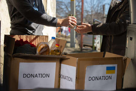 Cropped photo of a volunteer giving food to a refugee man standing near the car with many boxes of donation things inside the car.の写真素材
