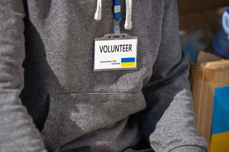 Cropped photo of volunteer young man with badge for helping ukranian people refugees sitting near the boxes with the food.の写真素材
