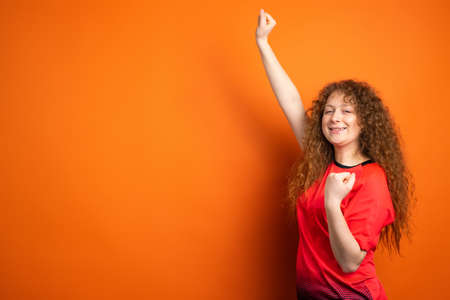Fan football redhead woman in red t-shirt uniform keeping fist raising hand up and another hand benting at the elbow.の写真素材