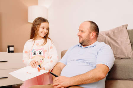 Little girl together with her father spending wonderful day at home she wants to show him a paper she draw something.の写真素材