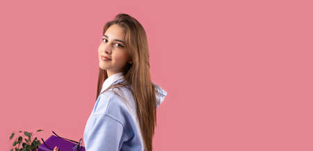 Picture of a young beautiful smiling student girl with blond long hair and make-up looking at the camera over her shoulder on pink background and copy space.の写真素材
