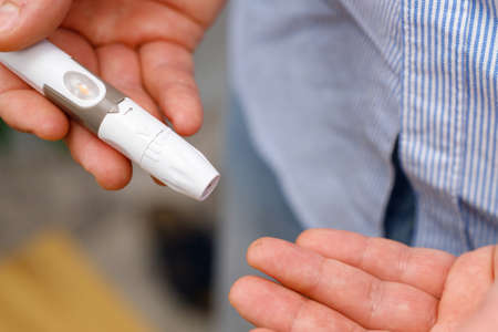 Close up photo of a man using lancet on finger for checking blood sugar level by glucose meter, glycemia and diabetes concept.の写真素材
