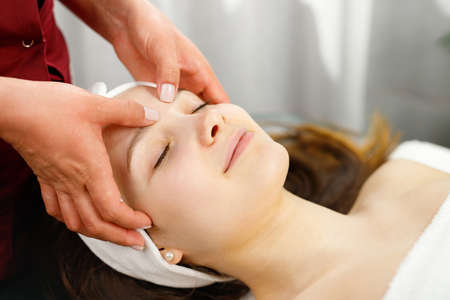 Close up photo of a beautiful relaxed woman undergoing acupressure facial massage in spa salon, health and beauty care concept.の写真素材
