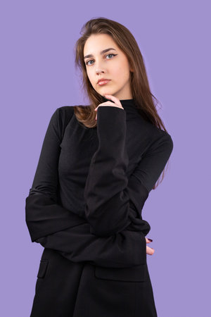 Young stylish business girl wearing black color clothes posing with expressive look keeping her hand on her chin on purple background.の写真素材