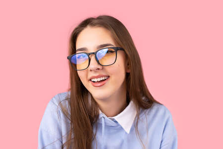 Close up photo of a beautiful young studewnt girl in glasses smiling and looking at the camera posing on pink background.の写真素材