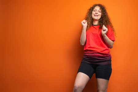 Joyful dancing redhead woman in favourite football team uniform posing on orange background, football fan emotions concept.の写真素材