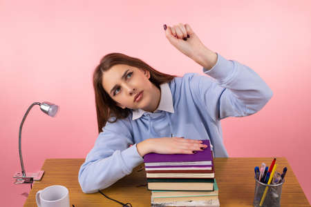 Young teenage school girl sitting at the table titled her head on her shoulder on hand keeping on the books and another hand clenches into a fist raises up.の写真素材