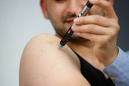 Cropped photo of a man with syringe making insulin injection to himself at home, diabetes and health care concept.の写真素材
