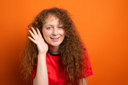 Close up photo of a beautiful redhead woman fan football in red t-shirt team uniform holding her palm on her ear to hear sounds of victory.の写真素材