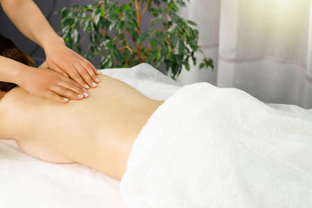 Young woman lying on the massage table in spa salon undergoing massage relax body procedure, concept of massage spa treatments.の写真素材