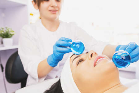 Cropped photo of professional specialist young woman on facial massage with ice ball cold globe. Anti wrinkle rejuvenation procedureの写真素材