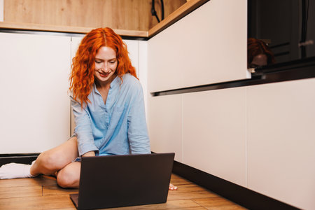 Young woman working from home office. Freelancer using laptop and the Internet for shopping online. Happy girl smiling. Workplace in cozy kitchen. Successful female business.の写真素材