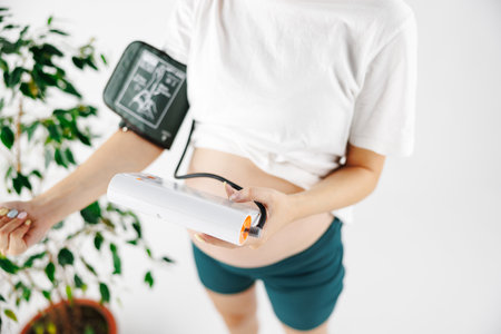 A woman measures blood pressure with an electronic pressure gauge, headache during pregnancy, poor health. selective focus on medical equipmentの写真素材