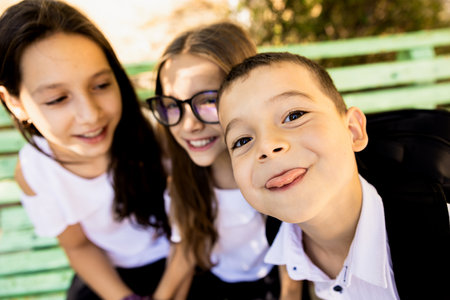 Three very happy children on the first day of school. The boy in the foreground shows his tongue at the camera.の写真素材