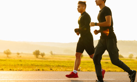 Two athletes running at sunset. Backlit silhouette of two friends training together.の写真素材