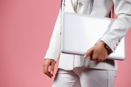 A woman in white clothes is holding her personal computer on a pink background.の写真素材