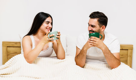 Loving couple watching TV in bed and drinck a cup of coffee. The concept of love and romance. Toning.の写真素材