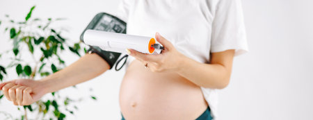 Happy pregnant girl sitting on the bed and measures blood pressure and stroking her tummy.の写真素材