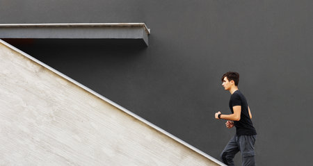 Silhouette of man running sprinting on road. Fit male fitness runner during outdoor workout with grey backgroundの写真素材
