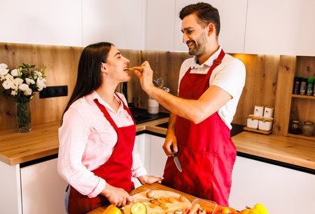 Young cheerful multi-ethnic couple preparing pasta together at their modern kitchen, having funの写真素材