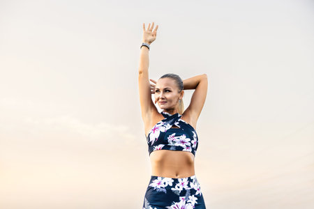 Young female workout before fitness training session at the park. Healthy young woman warming up outdoors. She is stretching her arms and looking away,hi key.の写真素材
