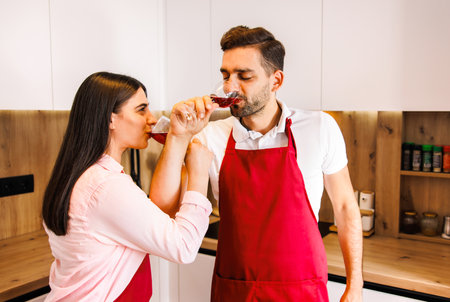 Happy young couple in love hugging holding glasses, drinking wine, celebrating Valentines day dining at home together, having romantic dinner date with candles sitting at table, embracing and bonding.の写真素材