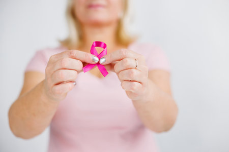 Woman in pink sweater with pink ribbon supporting breast cancer awareness campaignの写真素材