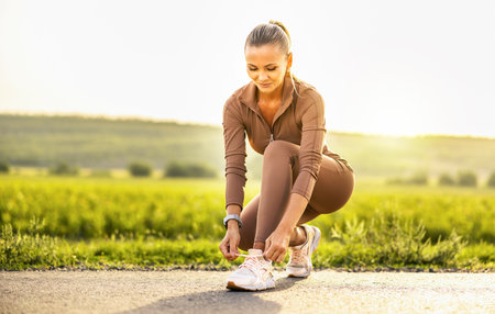 Young athlete. Beautiful girl athlete tying shoelaces on sneakers. Beautiful girl athlete sitting tying shoelaces on white sneakers. Healthy lifestyle concept.の写真素材