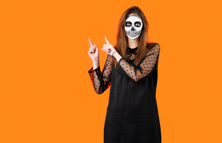 Clown happy man wearing black costume and halloween makeup looking at camera isolated over yellow background showing peace gesture holding pumpkin.の写真素材
