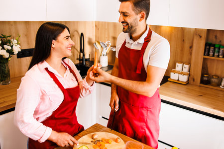 Romantic affectionate beautiful young couple holding glasses standing in modern cozy white kitchen room interior, happy married guy husband and girl wife drinking red wine celebrate together at homeの写真素材