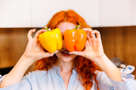 Happy young woman holding red pepper and yellow pepper. Young woman doing glasses with red and yellow peppers. Fresh vegetables, healthy eating, vegetable diet concept.の写真素材