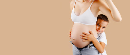Portrait of beautiful pregnant woman and her cute child, isolated image on beige background, back litの写真素材