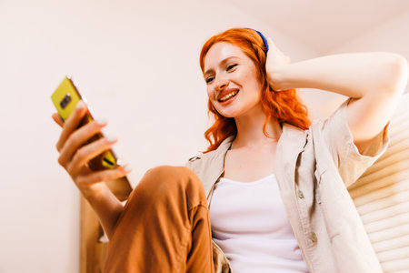 Young happy woman with orange hair using smart mobile phone with headphone for listen music.の写真素材