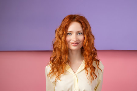 Portrait of young beautiful ginger woman with freckles cheerfuly smiling looking at camera. Isolated on pastel pink and purple background. Copy spaceの写真素材