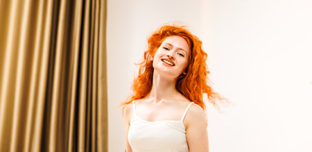 Portrait of woman with wavy orange hair looking into room with morning light. Lifestyle gorgeous lady feeling happy with soft light while smilingの写真素材